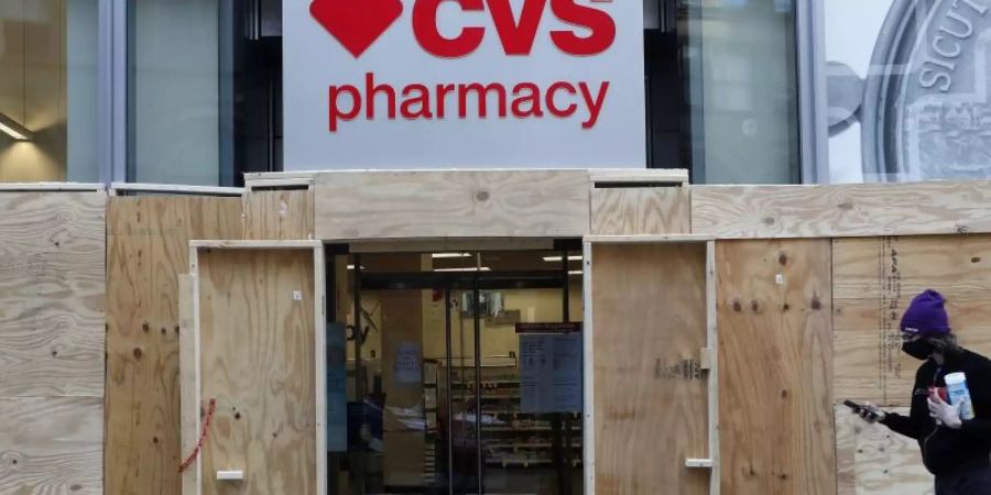 Ein Mann geht in Boston an einem mit Brettern vernagelten Geschäft der CVS-Apotheke vorbei. (Archivbild). Foto: Michael Dwyer/AP/dpa