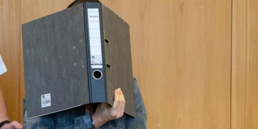 Die Angeklagte verdeckt ihr Gesicht mit einem Aktenordner, während sie in Handschellen in den Schwurgerichtssaal des Landgerichts in Ulm geführt wird. Foto: Stefan Puchner/dpa