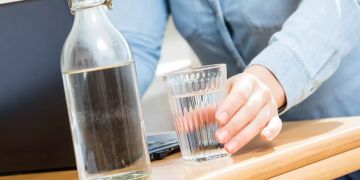 Hand mit Wasserglas auf Tisch, Wasserflasche