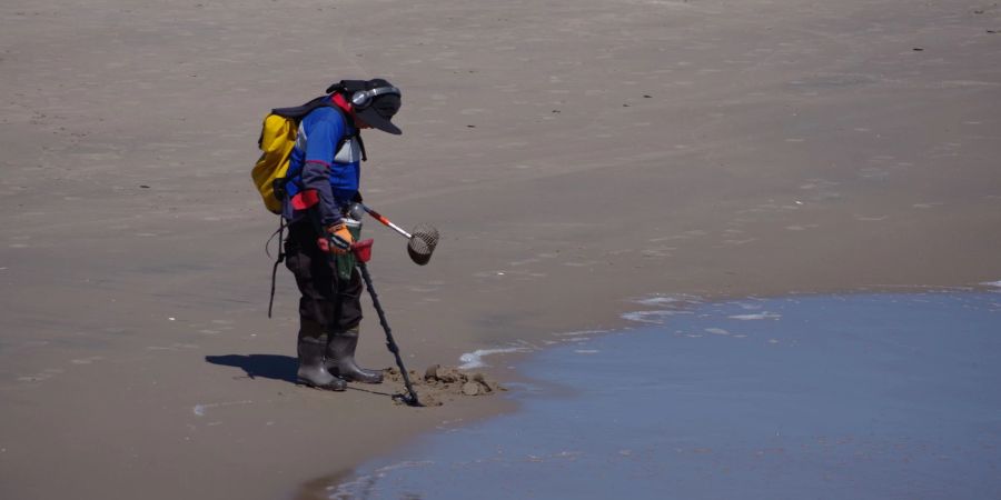 George Pessard mit einem Metalldetektor, Gummistiefeln, einem Sieb und zwei Plastikbehältern am Strand von Coney Island.