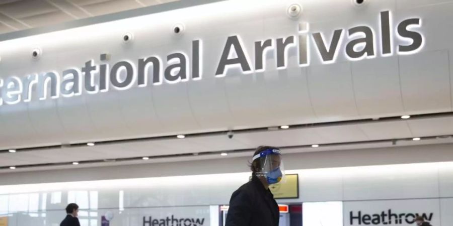 Ein Fluggast mit Mundschutz und Visier geht durch den Flughafen Heathrow. Foto: Matt Dunham/AP/dpa