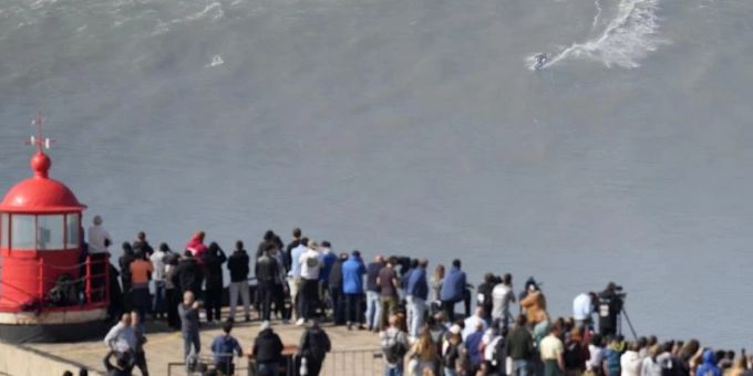Menschen am Leuchtturm bei Nazaré beobachten einen Surfer am Praia do Norte, der eine Riesenwelle surft. Foto: Armando Franca/AP/dpa Menschen am Leuchtturm bei Nazaré beobachten einen Surfer am Praia do Norte, der eine Riesenwelle surft. Foto: Armando Franca/AP/dpa