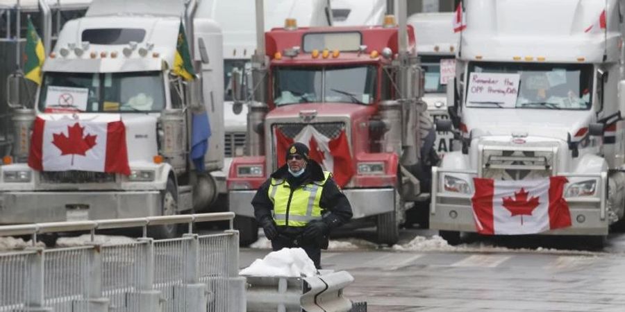 Ein Polizeibeamter steht vor Lastwagen, die die Strassen der Innenstadt von Ottawa blockieren. Foto: Patrick Doyle/The Canadian Press/AP/dpa