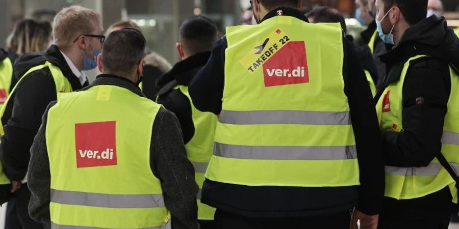 Eine Gruppe Streikender mit gelben Verdi-Westen versammelt sich im Köln-Bonn-Airport (Februar). Foto: David Young/dpa