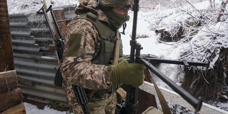 Ein ukrainischer Soldat trägt in einem Graben an der Frontlinie in der Ostukraine ein schweres Maschinengewehr. Foto: Vadim Ghirda/AP/dpa