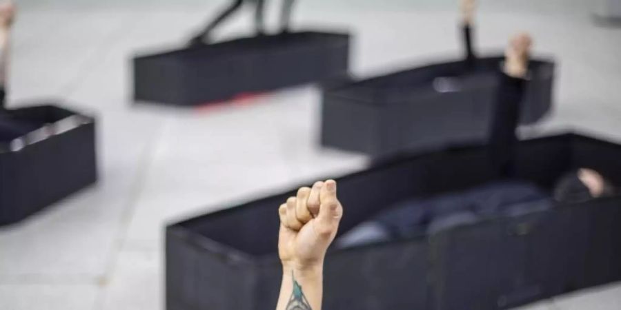 Frauen heben ihre Fäuste, während sie bei einer Demonstration im Vorfeld des Internationalen Frauentages vor dem Bundesgericht von Tel Aviv in Särgen liegen. Die Särge repräsentieren Frauen, die durch häusliche Gewalt getötet wurden. Foto: Ariel Schalit/AP/dpa