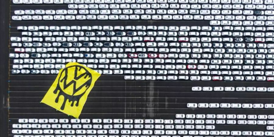 Greenpeace-Aktivisten breiten ein riesiges Protesttransparent über Autos aus, die auf dem Verladeplatz von VW im Emdener Hafen stehen. Foto: Greenpeace/dpa