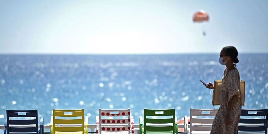 Eine Frau geht auf der Strandpromenade an der französischen Riviera an Stühlen vorbei. Foto: Anne-Christine Poujoulat/AFP/dpa