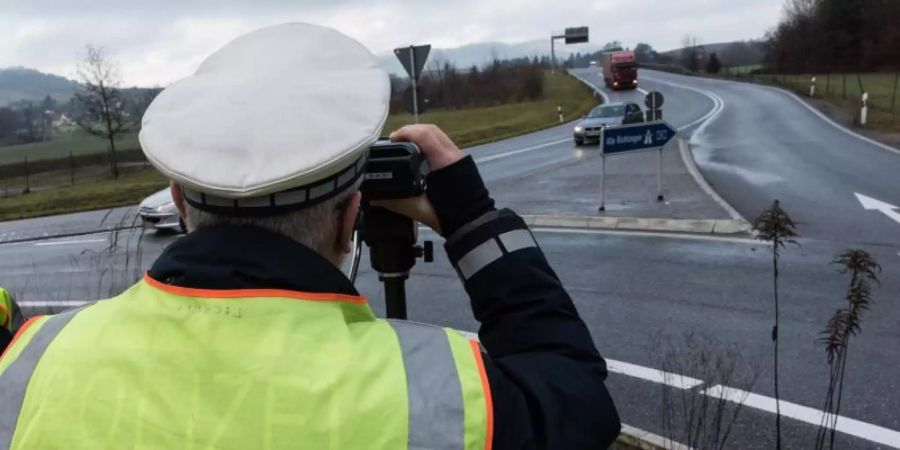 Ein Polizist misst die Geschwindigkeit passierender Autos. Die neuen Rgelungen des Bussgeldkatalogs für Verkehrssünder sind wegen eines Formfehlers zurzeit in Teilen ausser Vollzug gesetzt. Foto: picture alliance / Patrick Seeger/dpa