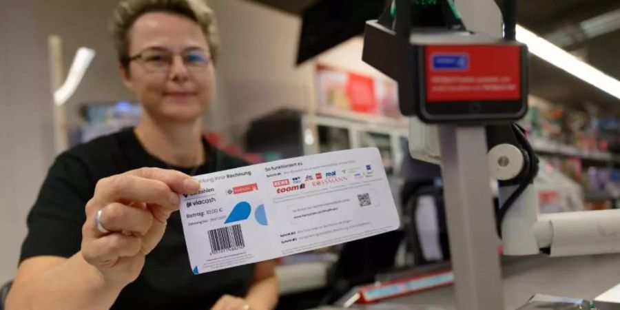 Eine Mitarbeiterin in einer Filiale des Einzelhändlers REWE hält ein Blatt mit einem Barcode in der Hand. Mit diesem Abschnitt sollen Bürger in Köln ihre Knöllchen künftig einfach an Supermarktkassen begleichen können. Foto: Henning Kaiser/dpa