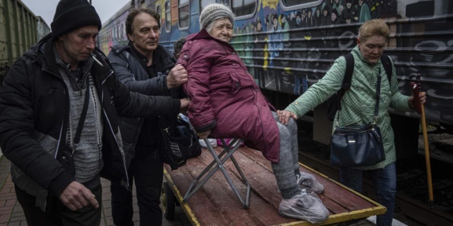 Angehörige einer älteren Frau transportieren sie zu einem Evakuierungszug in Cherson. Foto: Evgeniy Maloletka/AP/dpa