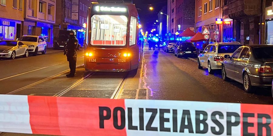 Ein Polizist steht mit einer Maschinenpistole hinter einer Polizeiabsperrung.