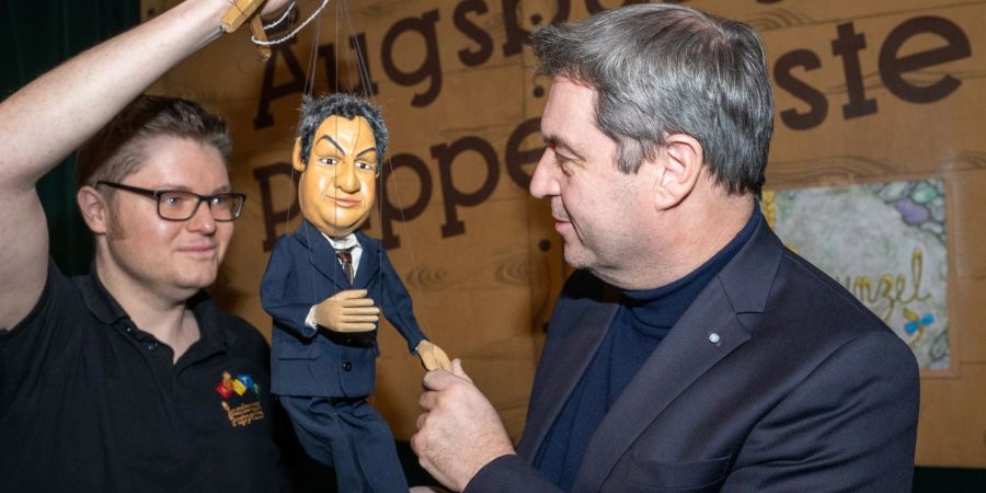 Markus Söder (r, CSU), Ministerpräsident von Bayern, gibt in der Augsburger Puppenkiste einer Söder-Marionette die Hand.