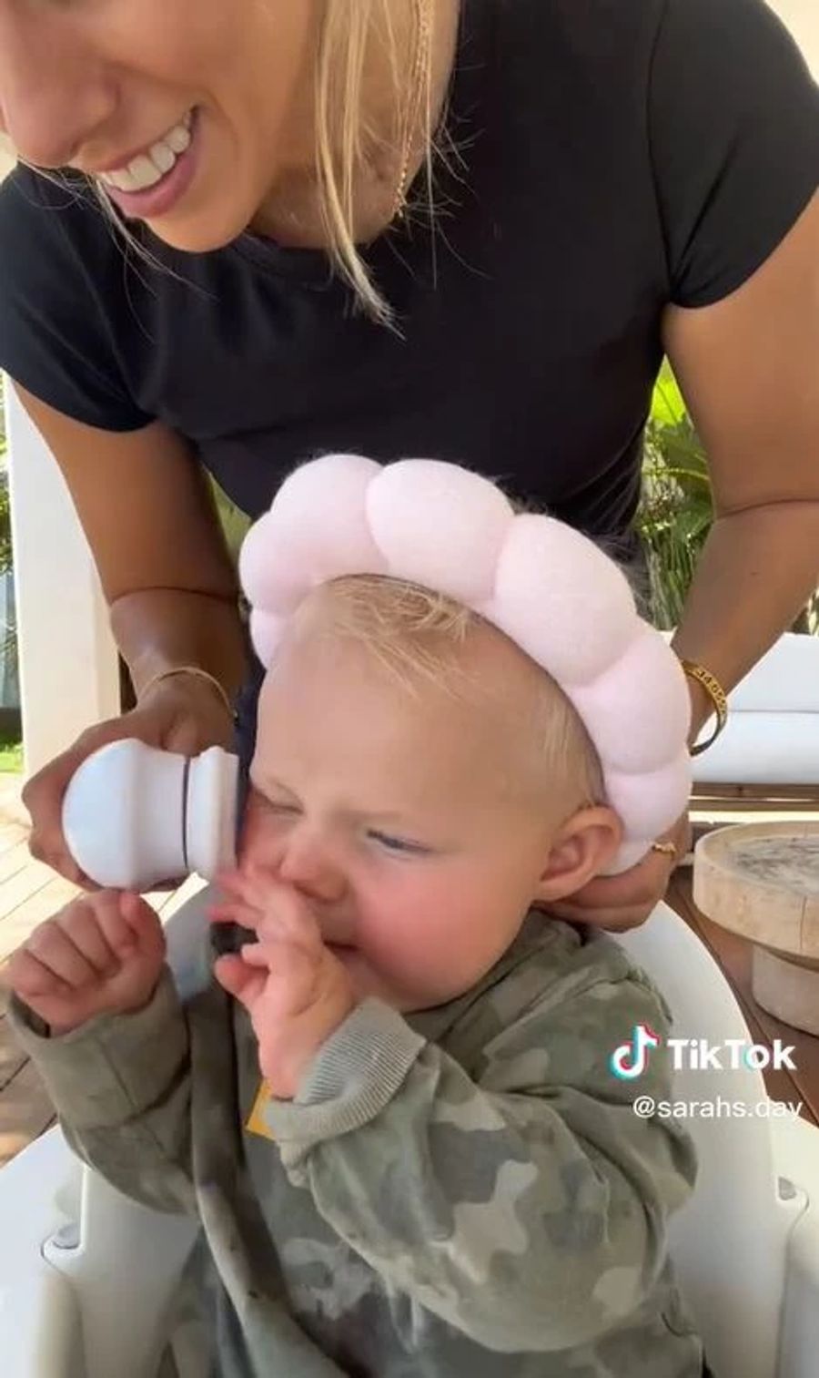 Eine Mama gibt ihrem kleinen Sohn eine Gesichtbehandlung mit einer elektrischen Bürste. Der Kleine wirkt nicht sehr erfreut.