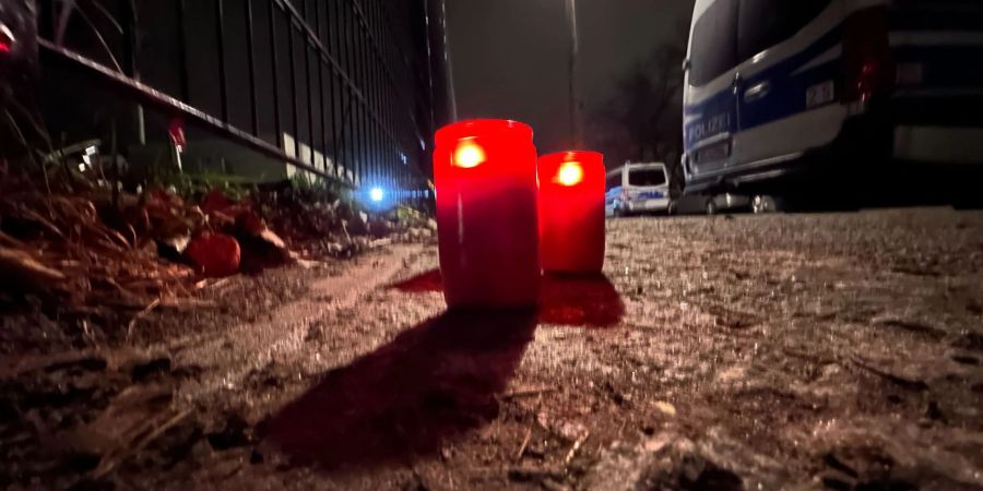 Brennende Kerzen stehen an einem Park in Pankow neben Polizeifahrzeugen. Nach dem Tod des Mädchens legten Menschen in der Nähe des Fundortes auch eine gelbe Blume und ein kleines Kuscheltier ab.