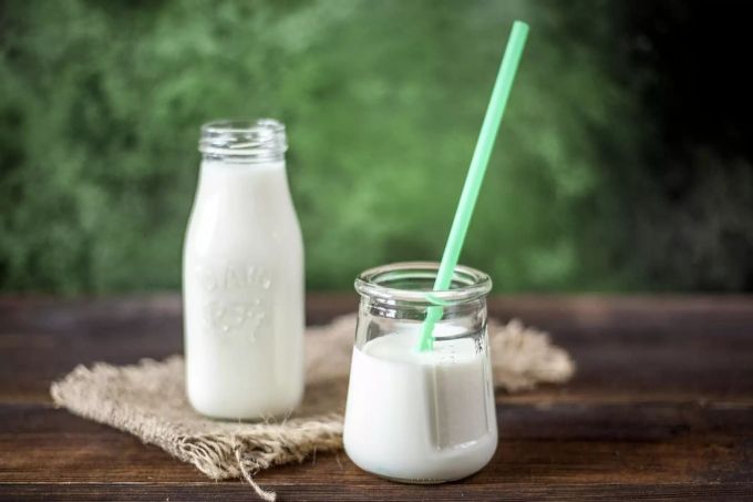 Ein Glas mit Röhrchen und eine Flasche Milch stehen auf einem Holztisch. Milch
