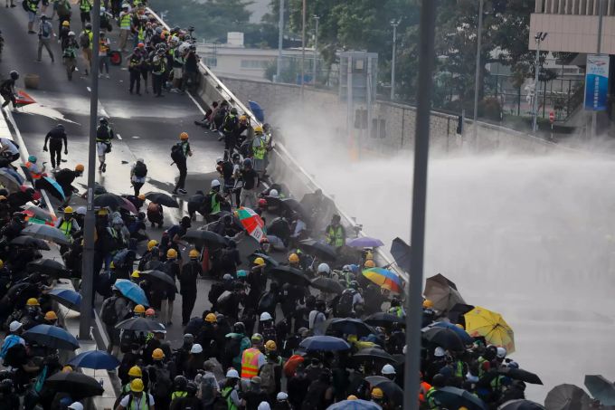 Demonstranten, die Regenschirme tragen, ziehen durch die Strassen, während die Polizei Wasserwerfer einsetzt. Proteste in Hongkong