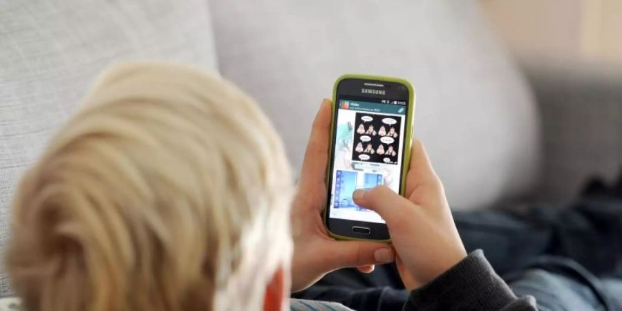 Ein Kind liegt auf einem Sofa und blickt auf sein Smartphone. Foto: Tobias Hase/dpa/Illustration