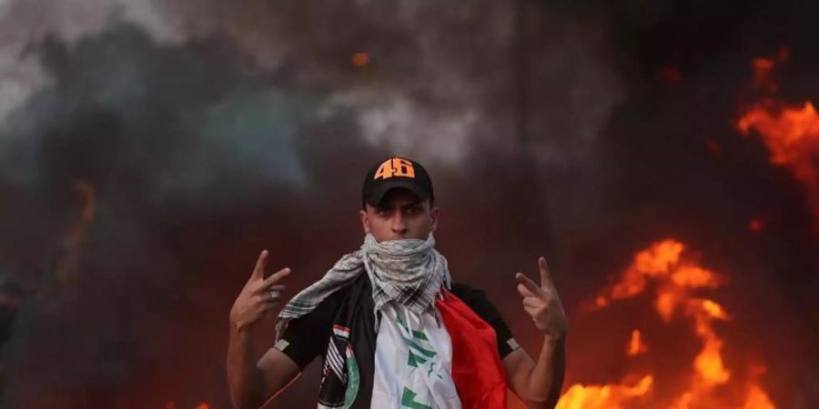 Ein Demonstrant zeigt vor lodernden Flammen das Siegeszeichen. In mehreren Provinzen stürmten die Protestler Gebäude und legten Feuer. Viele Iraker klagen über die vernachlässigte Infrastruktur sowie über die Arbeitslosigkeit. Foto: Hadi Mizban/AP/dpa