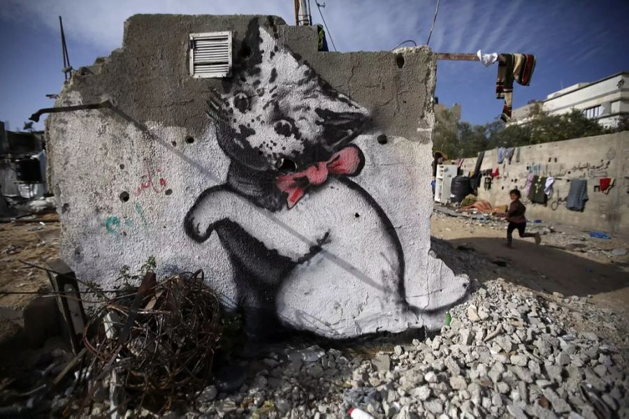 Ein Banksy-Grafiti einer Katze, die mit einem Schrottknäuel spielt.