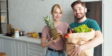 Mann und Frau mit Einkaufstüten voller Obst und Gemüse.