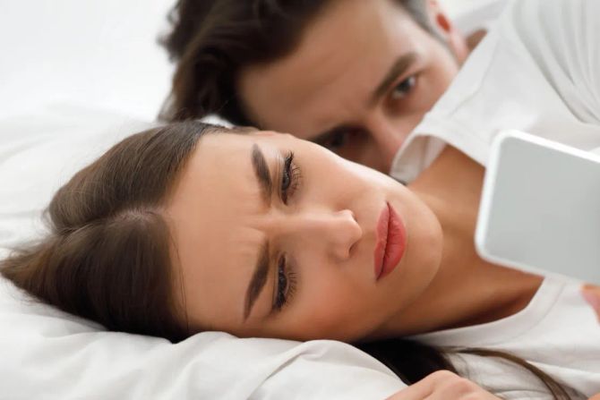 Frau mit Handy im Bett, Mann dahinter