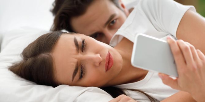 Frau mit Handy im Bett, Mann dahinter