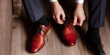 Mann zieht braune Lederschuhe an.