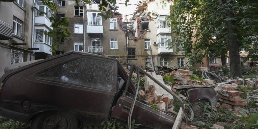 ARCHIV - Ein Autowrack ist nach einem Angriff vor einem beschädigten Wohnhaus in Sumy zu sehen. Foto: Andrii Marienko/AP/dpa/Archivbild