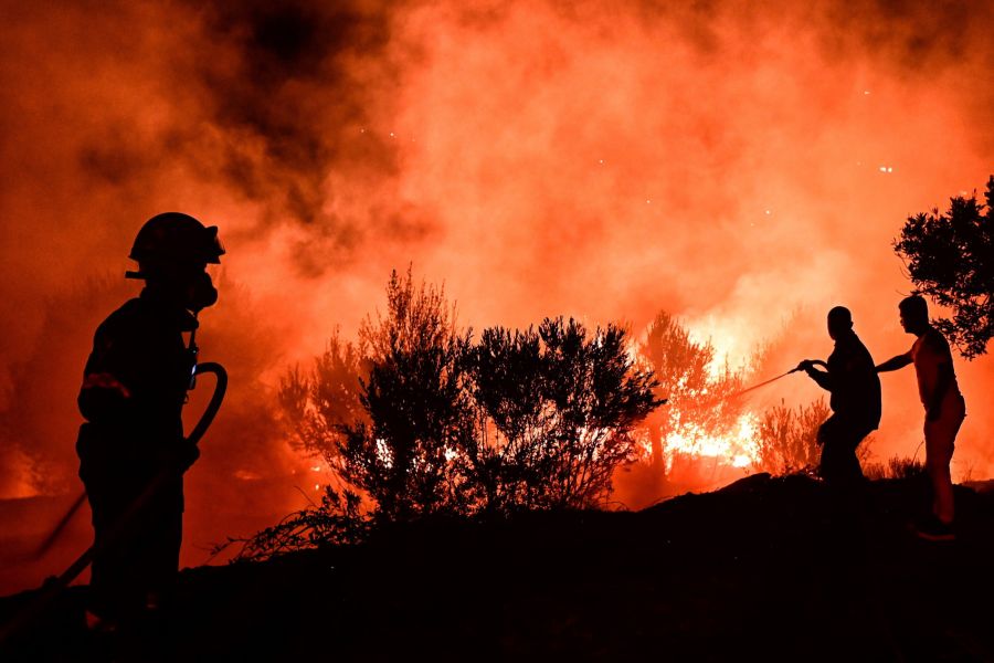 Ein Feuerwehrmann und Freiwillige bekämpfen in der Nacht die Flammen nahe Athen mit einem Schlauch.