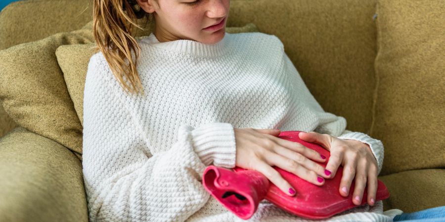 Frau mit Wärmflasche auf der Couch