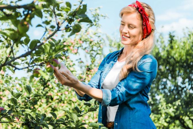 Lächelnde Frau berührt Obstbaum im Garten