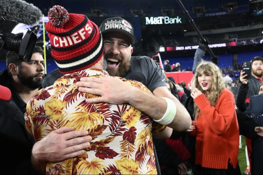 Ein unzertrennliches Bruderpaar: Travis Kelce umarmt seinen Bruder Jason, Taylor Swift beobachtet sie im Hintergrund.