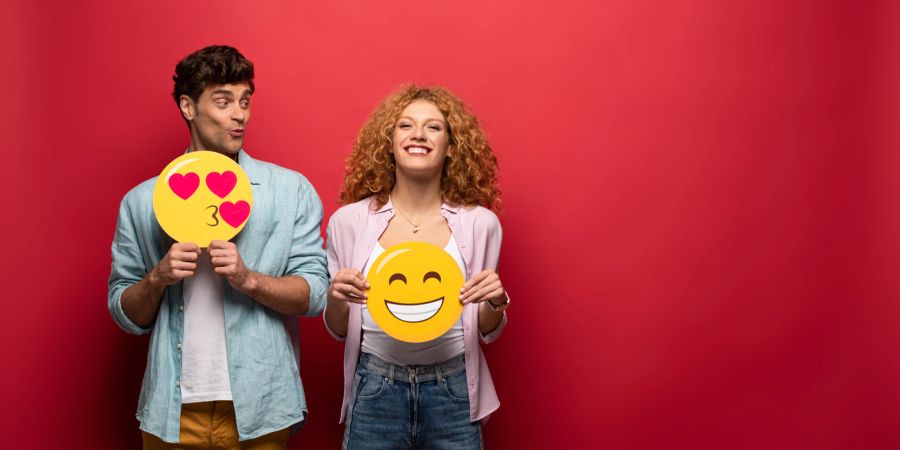 mann und frau vor rotem hintergrund, halten emojis in den händen, lachen