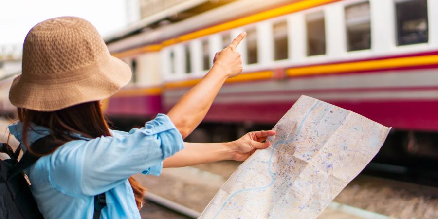 Alleinreisende Backpackerin auf einem Bahnsteig mit Landkarte.