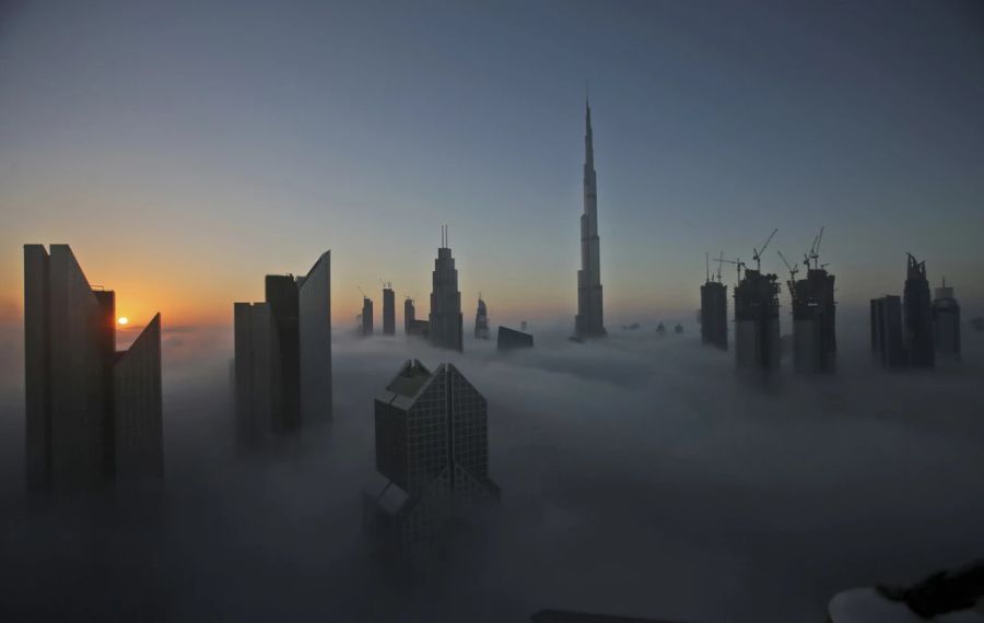 Sonnenaufgang über der Skyline von Dubai (VAE), mit dem Burj Khalifa im Hintergrund, fotografiert vom Balkon im 42. Stock eines Hotels am nebligen Sylvestermorgen von 2016.