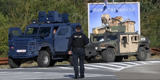 Bewaffnete Kosovo-Polizisten sichern eine Strasse, während im Hintergrund ein Militärfahrzeug der Kosovo Force (KFOR) zu sehen ist, in der Nähe des Dorfes Banjska, Kosovo, 26. September 2023.