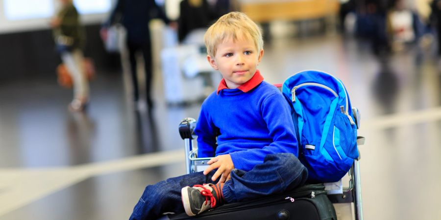Kleiner Junge wartet am Flughafen mit Gepäck.