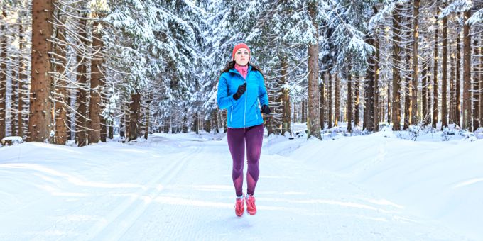 Trotz Erkältung im Schnee joggen? Möglich, aber man sollte sich dabei nicht überfordern. Frau joggt im Schnee