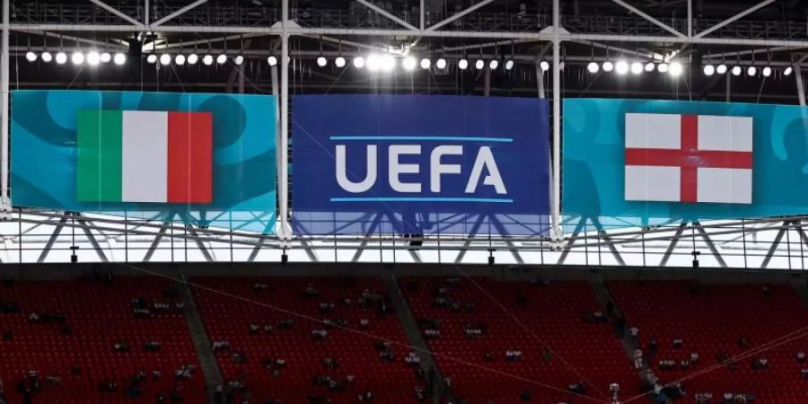 Das Logo der UEFA hängt vor dem EM-Finale zwischen den Fahnen von Italien und England über der Tribüne. Foto: Christian Charisius/dpa