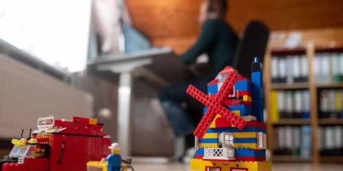 Ein Mann arbeitet im Homeoffice, während im Vordergrund Spielzeug seiner Kinder steht. mann kinder homeoffice