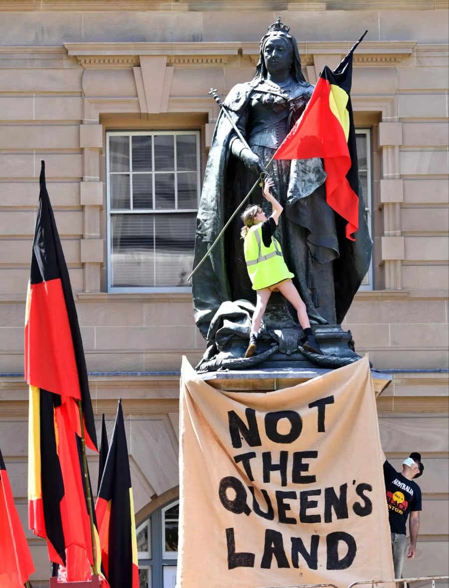 Die Protestler nennen den Tag auch «Invasion Day», hier hängt ein Demonstrant eine Flagge der Aborigines an die Statue von Königin Victoria in Brisbane.