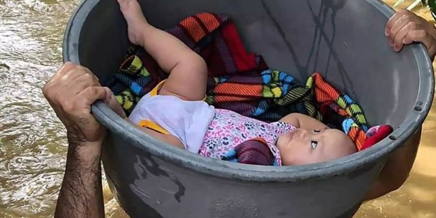 Ein Mann trägt ein Baby in einem Plastikbehälter. Der Taifun «Vamco» hat auf den Philippinen schwere Verwüstungen angerichtet. Foto: Uncredited/Philippine Coast Guard/AP/dpa