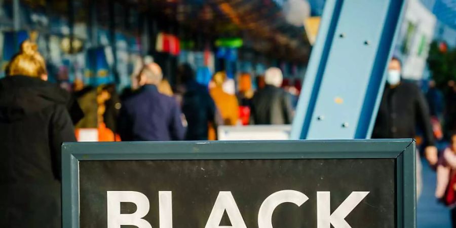 Passanten gehen vor einem Einkaufszentrum an einem Schild vorbei, das auf «Black Friday»-Angebote hinweist. Menschenmassen in Einkaufsstrassen und drohende Verstösse gegen Corona-Regeln: In den Niederlanden lehnen sich Städte gegen die Verkaufsaktion «Black Friday» auf. Foto: Marco De Swart/ANP/dpa