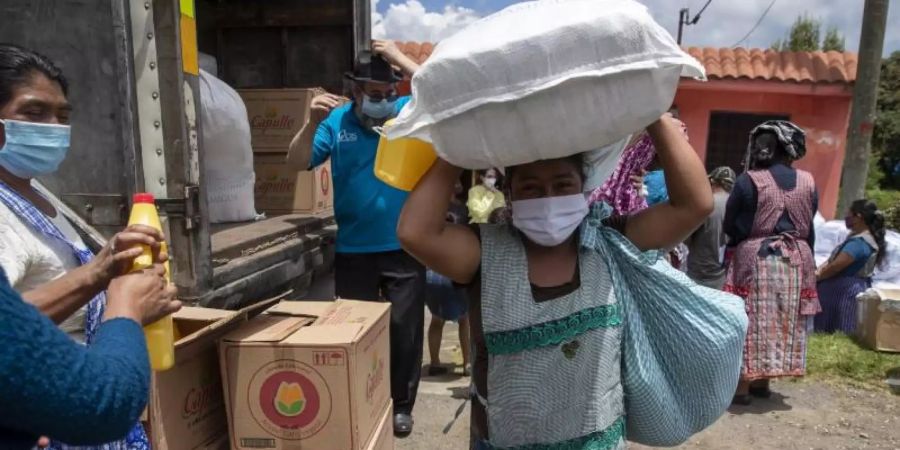 Eine Frau mit Mundschutz macht sich in San Jose Calderas, Guatemala, mit einem Sack voll Hilfsgütern auf den Heimweg. Foto: Moises Castillo/AP/dpa