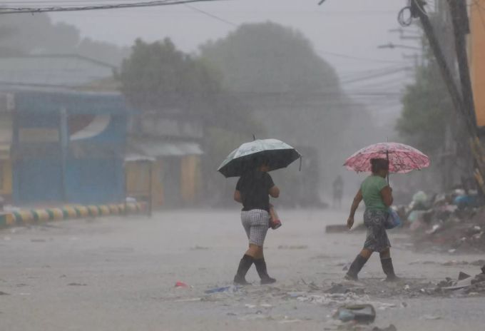 17.11.2020, Honduras, La Lima: Zwei Frauen gehen bei starkem Regen mit jeweils einem Regenschirm in der Hand über eine Strasse. Rund zwei Wochen nach dem verheerenden Hurrikan «Eta» hat ein zweiter gefährlicher Sturm in Mittelamerika Land erreicht. Als Hurrikan der Kategorie vier traf «Iota» auf Land. Hurrikan «Iota» - Honduras