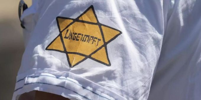 "Ungeimpft" steht auf einem nachgebildeten Judenstern am Arm eines Mannes, der versucht hatte, sich unter die Teilnehmer einer Demonstration in Frankfurt im Mai vergangenen Jahres zu mischen, die sich auch gegen Verschwörungstheorien zum Corona-Virus wendet. Foto: Boris Roessler/dpa "Ungeimpft" steht auf einem nachgebildeten Judenstern am Arm eines Mannes, der versucht hatte, sich unter die Teilnehmer einer Demonstration in Frankfurt im Mai vergangenen Jahres zu mischen, die sich auch gegen Verschwörungstheorien zum Corona-Virus wendet. Foto: Boris Roessler/dpa