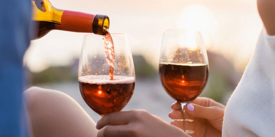 paar stösst mit wein an, sonnenuntergang