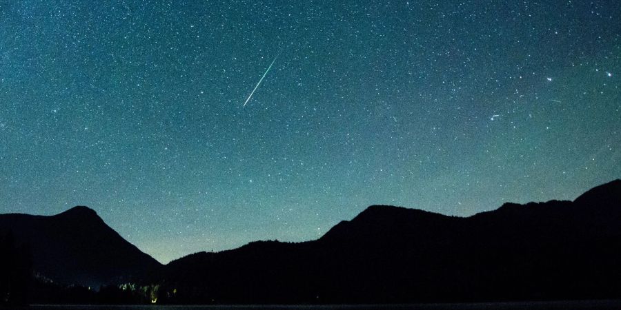 Eine Sternschnuppe leuchtet neben der Milchstrasse am Himmel über dem Walchensee.