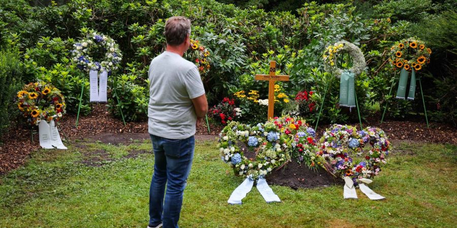 Ein Mann steht in stillem Gedenken an dem mit Kränzen und Blumen geschmückten schlichten Grab der Fussballlegende Uwe Seeler.